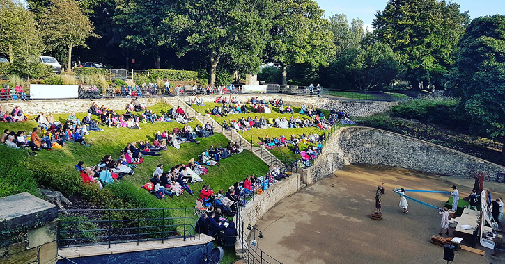 people sat outdoors in Wharton Park, Durham City watching a live performance